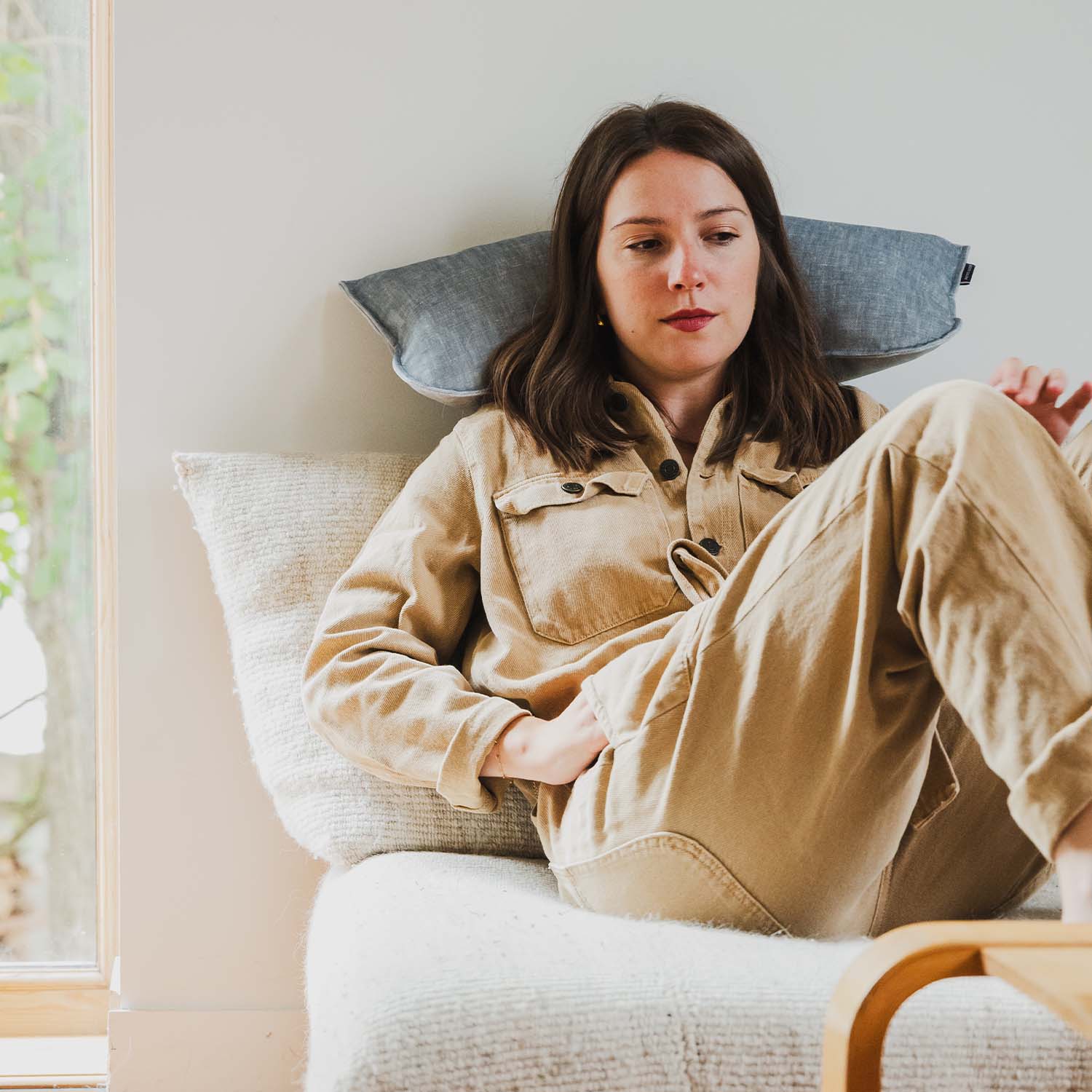 Femme assise sur canapé avec coussin cervical en velours bleu