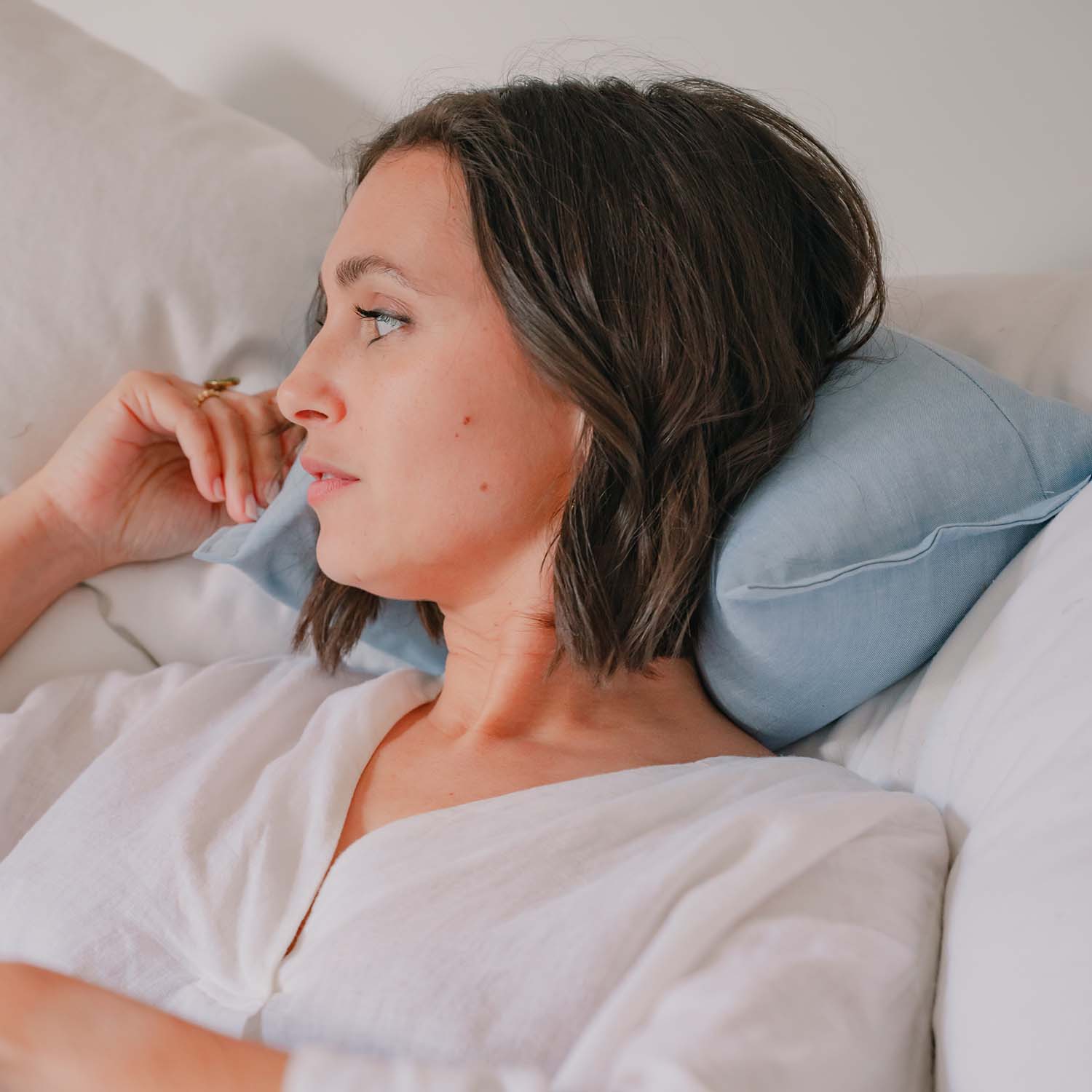 Femme confortablement installée sur son lit avec coussin cervical SALVADOR de Cosy Club, coloris bleu pastel, ambiance détendue et apaisante, couleurs douces