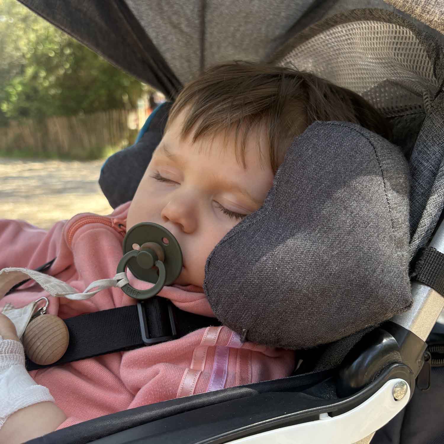 Enfant confortablement installé dans sa poussette pour dormi. Il a le coussin TEODOR de Cosy Club derrière le cou, la tête bien maintenue. Il dort profondément.