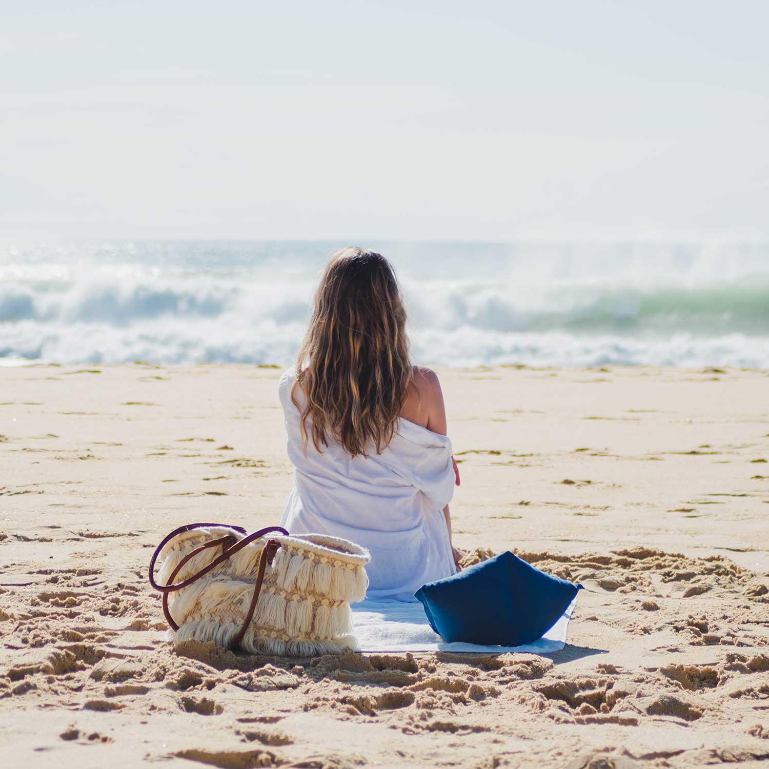Jeune femme assise sur la plage avec coussin cervical coloris bleu