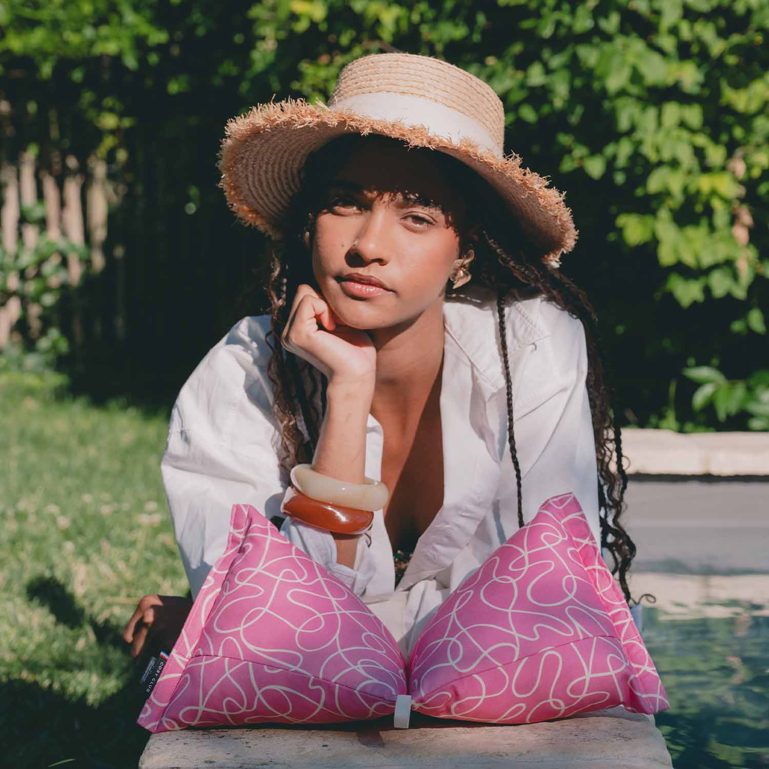 Femme allongée en bord piscine avec coussin cervical rose