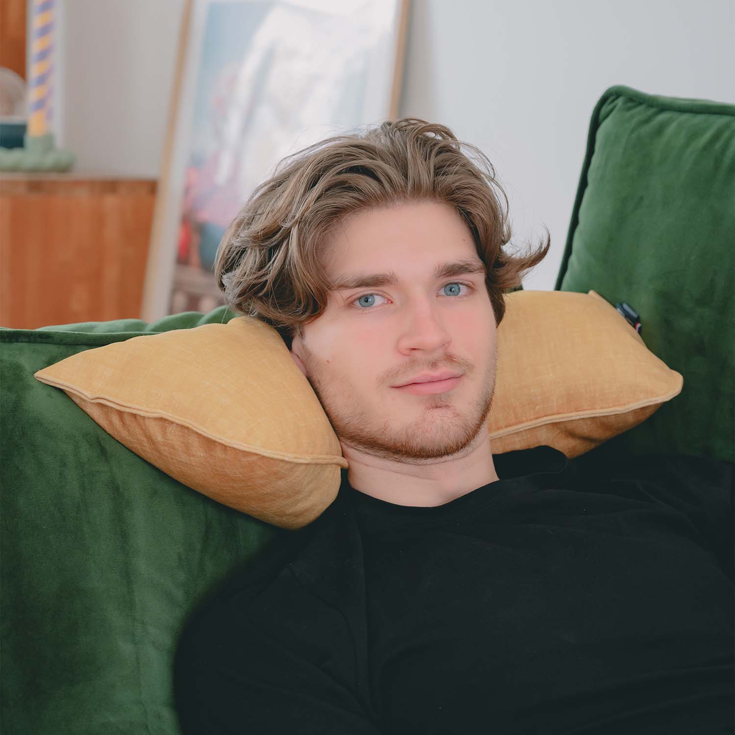 Homme allongé sur canapé vert avec coussin cervical en velours jaune