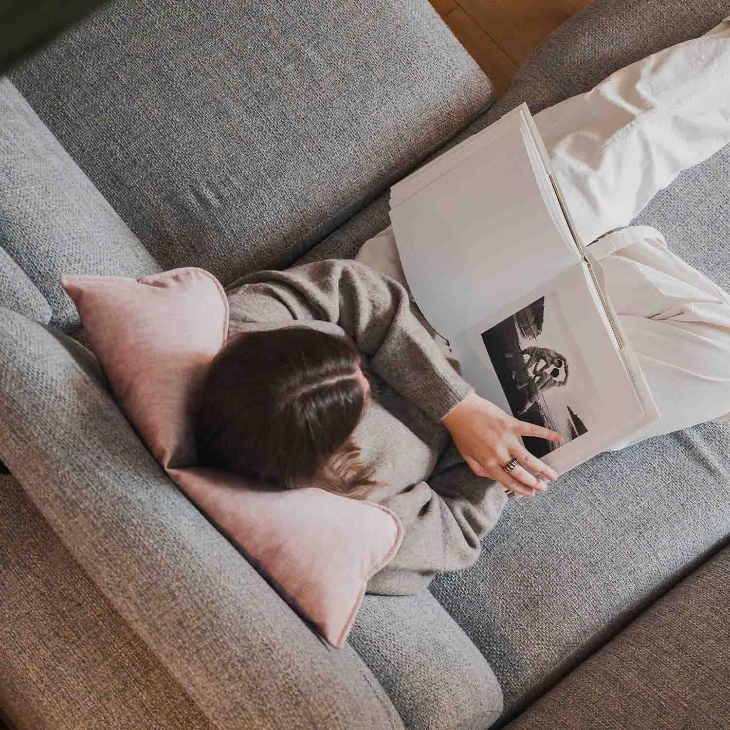 Femme assise sur canapé avec coussin cervical rose, vue plongeante