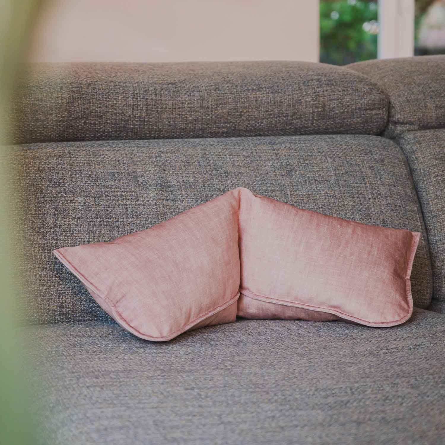 Coussin cervical rose poudré posé sur canapé gris