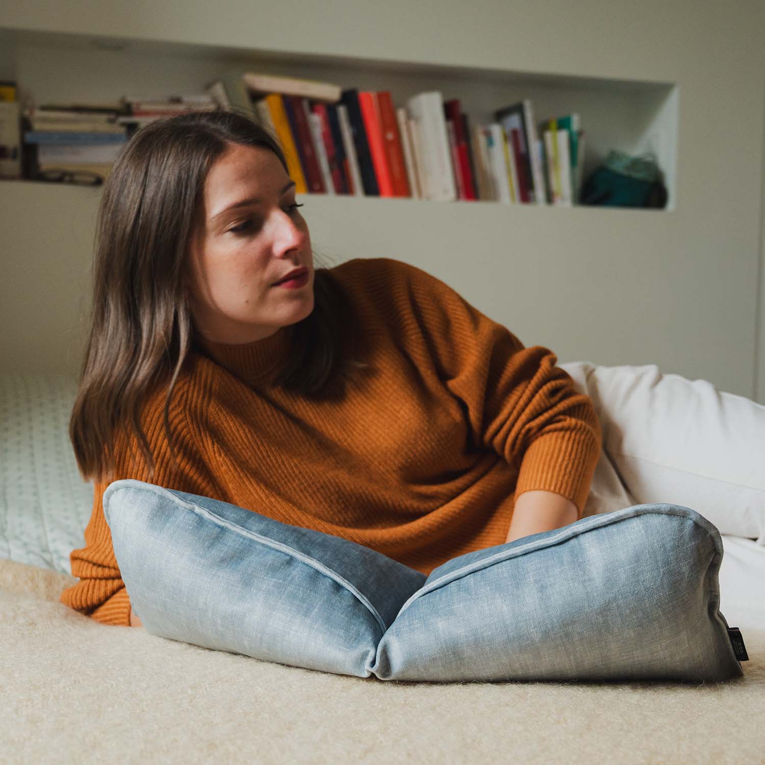 Femme allongée sur un lit avec coussin cervical en velours bleu