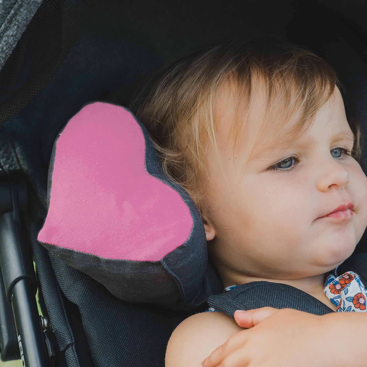 Enfant bien installée dans sa poussette avec le coussin de maintien de la tête TEODOR de Cosy Club. Tissu du coussin gris et cœur velours coloris rose.