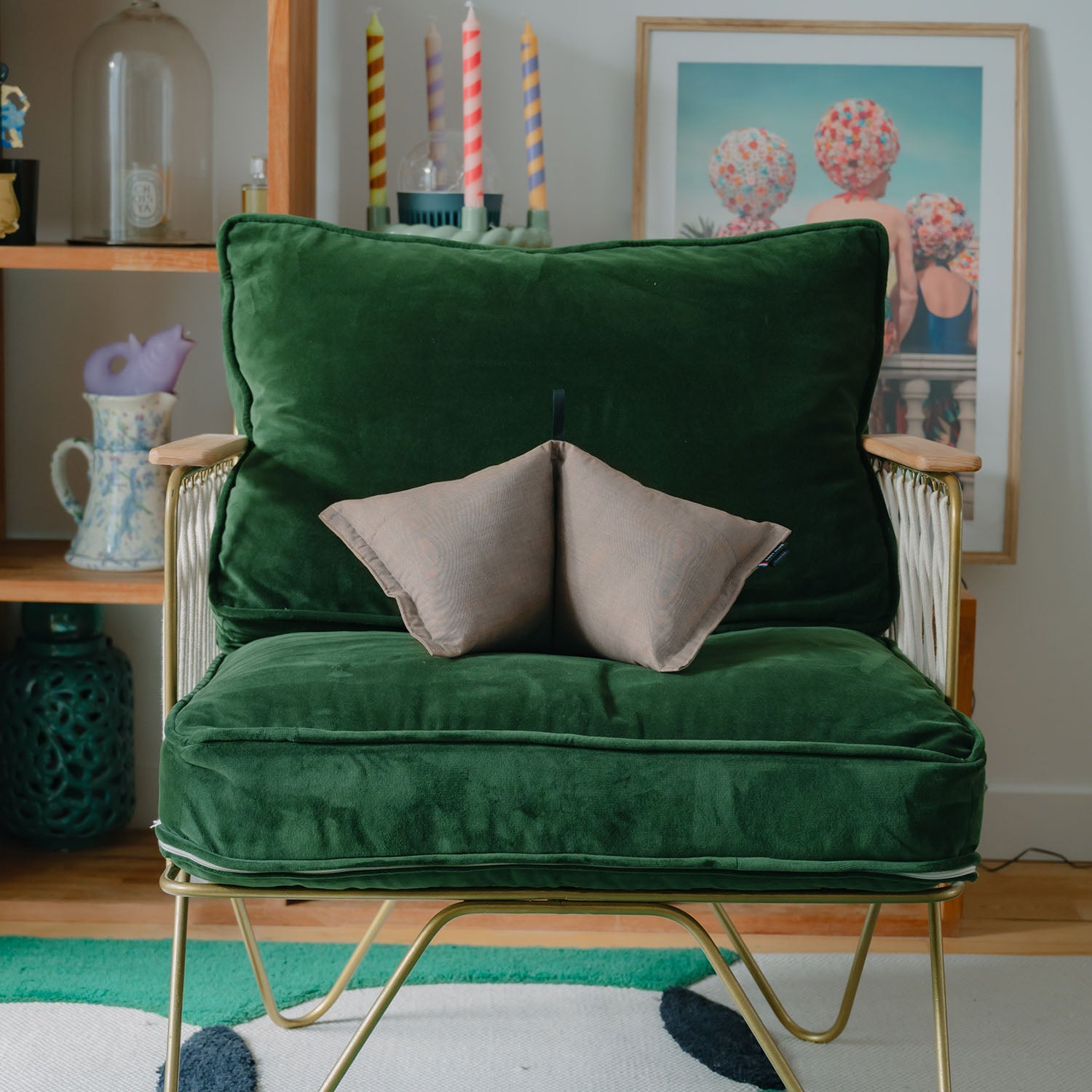 Un coussin de deco et de bien etre gris est posé sur un fauteuil vert en velours 